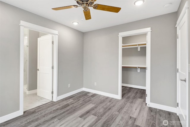 unfurnished bedroom with a spacious closet, ceiling fan, baseboards, wood finished floors, and a closet