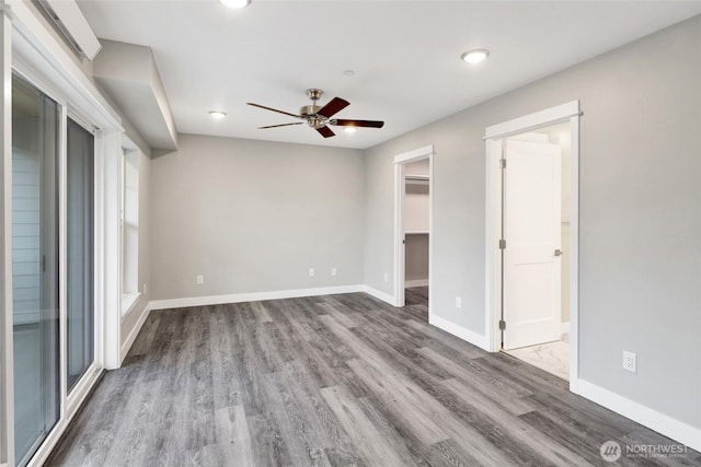 unfurnished bedroom featuring a walk in closet, baseboards, ensuite bath, and wood finished floors