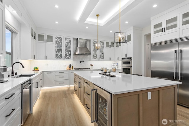 kitchen featuring a sink, a kitchen island, wine cooler, appliances with stainless steel finishes, and wall chimney exhaust hood