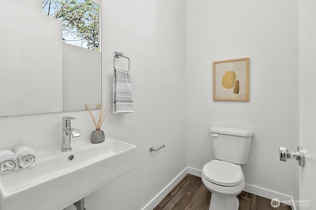 bathroom with toilet, wood finished floors, baseboards, and a sink