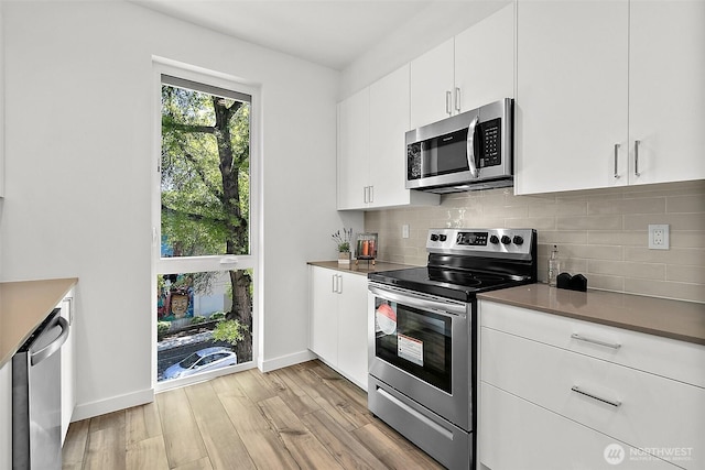 kitchen with light wood-style flooring, backsplash, white cabinetry, appliances with stainless steel finishes, and baseboards