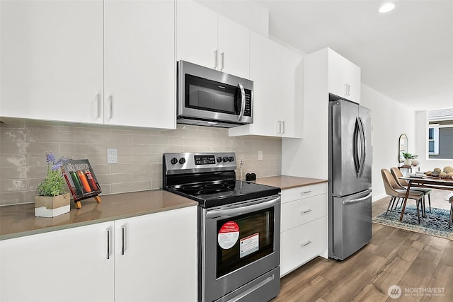 kitchen featuring tasteful backsplash, white cabinets, appliances with stainless steel finishes, and wood finished floors