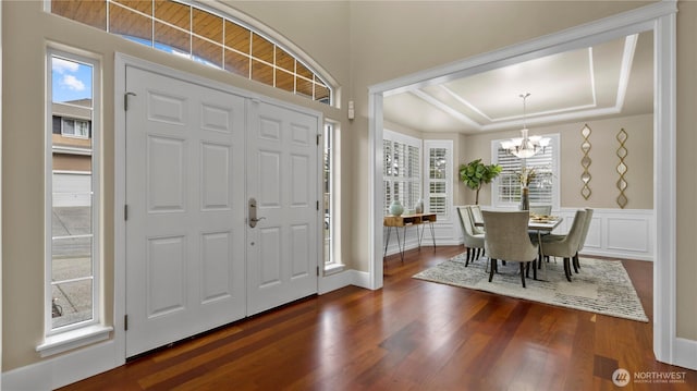 foyer featuring a tray ceiling, a notable chandelier, wainscoting, and dark wood-style flooring