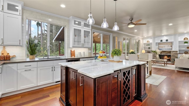 kitchen with dark wood finished floors, a fireplace, ceiling fan, a sink, and crown molding