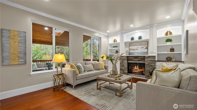 living area with a glass covered fireplace, baseboards, wood finished floors, and ornamental molding