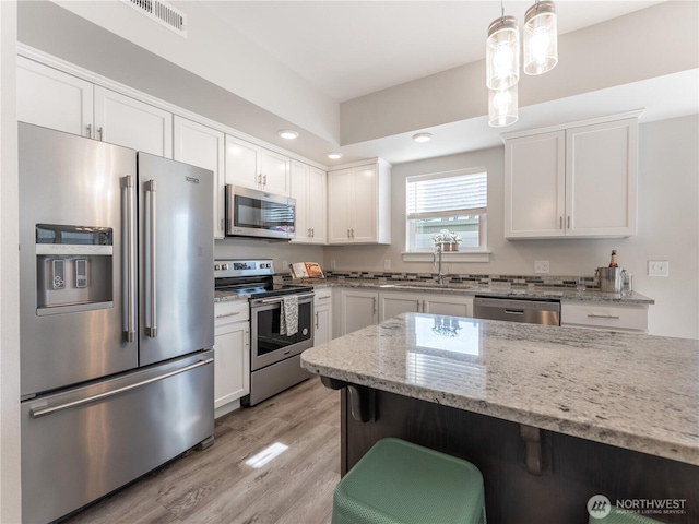 kitchen featuring light stone counters, visible vents, a sink, stainless steel appliances, and a kitchen bar