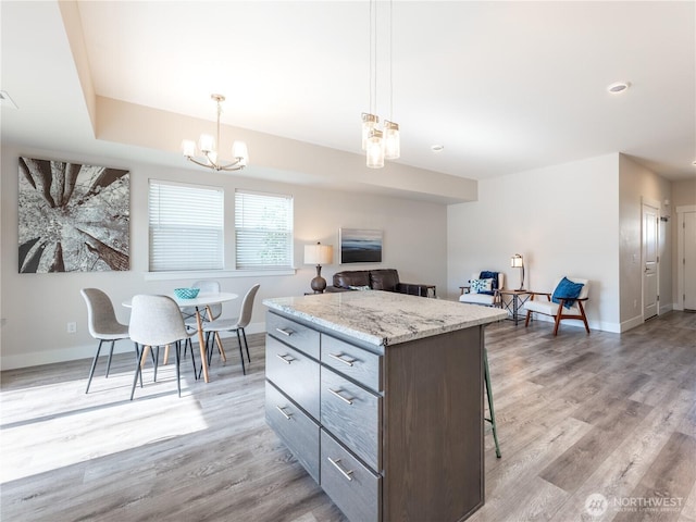 kitchen with a center island, baseboards, a chandelier, light wood-style flooring, and a kitchen breakfast bar