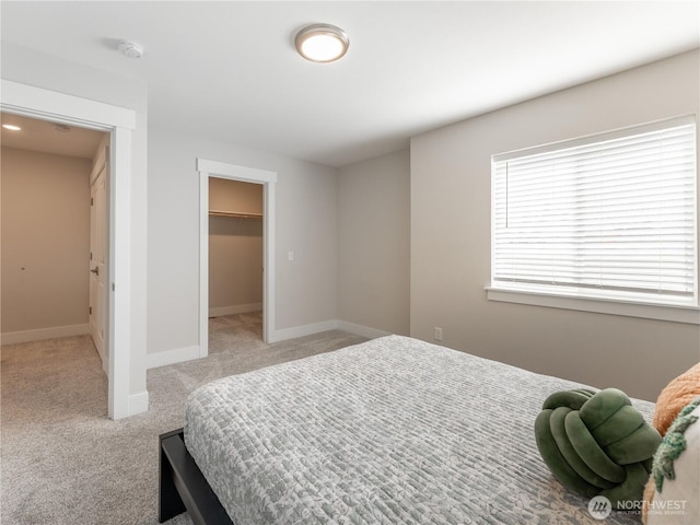 bedroom featuring a walk in closet, baseboards, a closet, and light carpet