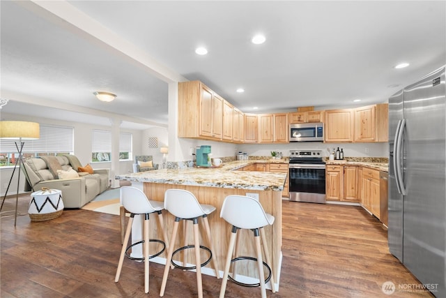 kitchen featuring open floor plan, appliances with stainless steel finishes, a peninsula, and light brown cabinetry