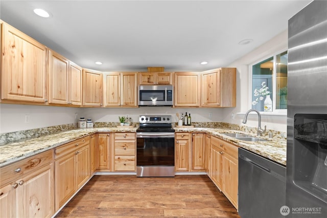 kitchen with light stone countertops, light brown cabinetry, appliances with stainless steel finishes, light wood-style floors, and a sink