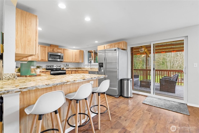 kitchen featuring light brown cabinets, light wood finished floors, a breakfast bar, a peninsula, and stainless steel appliances