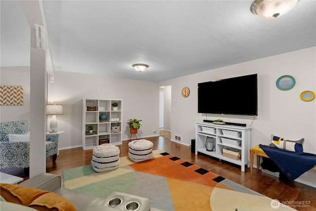 living area with visible vents, a textured ceiling, baseboards, and wood finished floors