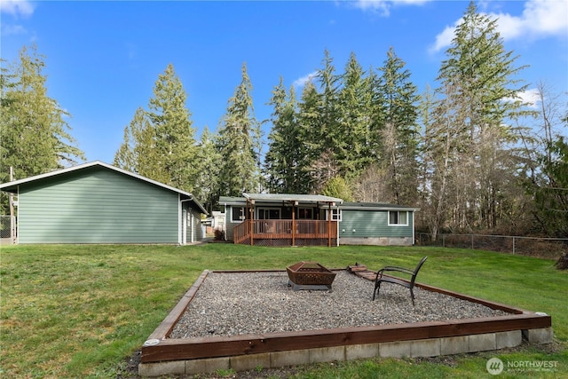 rear view of house with a wooden deck, a fire pit, a lawn, and fence