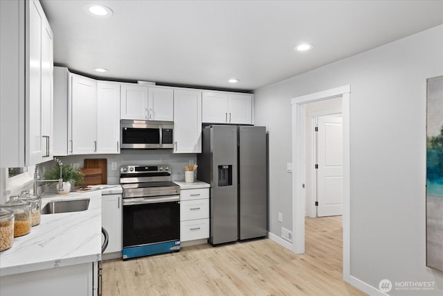 kitchen with white cabinetry, light stone countertops, light wood-type flooring, and stainless steel appliances