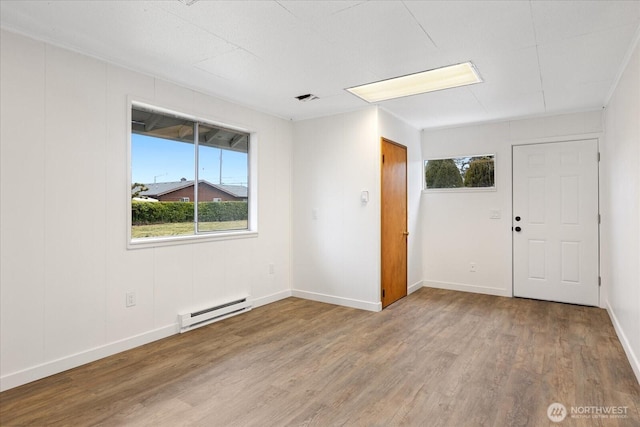 spare room featuring visible vents, wood finished floors, baseboards, and a baseboard radiator