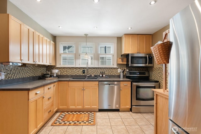 kitchen featuring appliances with stainless steel finishes, a sink, backsplash, dark countertops, and light tile patterned floors