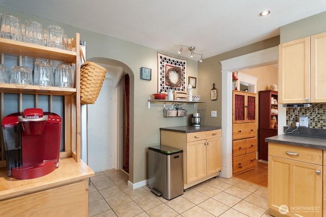 kitchen featuring arched walkways, light tile patterned floors, decorative backsplash, and dark countertops