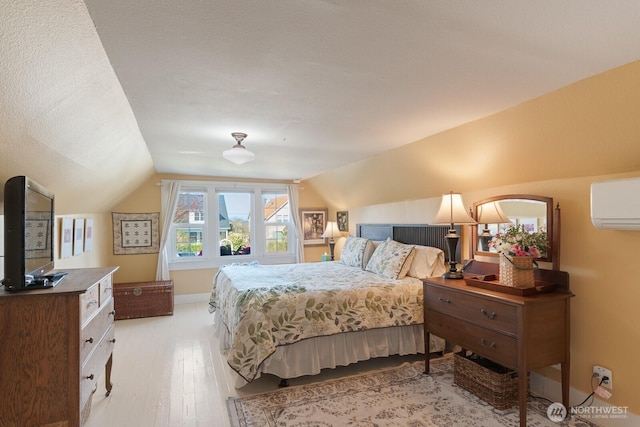 bedroom featuring vaulted ceiling, an AC wall unit, light wood-style flooring, and baseboards
