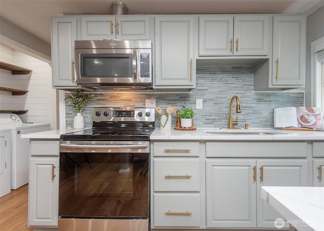 kitchen with a sink, tasteful backsplash, washing machine and dryer, appliances with stainless steel finishes, and light countertops