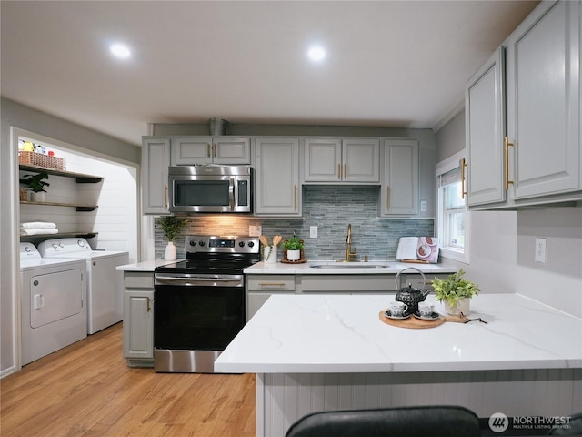 kitchen with washing machine and clothes dryer, light wood-style flooring, gray cabinets, a sink, and stainless steel appliances