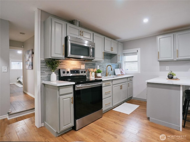 kitchen with a sink, stainless steel appliances, backsplash, and gray cabinetry