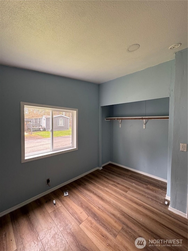 unfurnished bedroom with a textured ceiling, baseboards, and wood finished floors