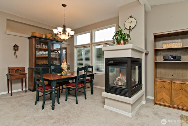 dining room with light carpet, a notable chandelier, baseboards, and a multi sided fireplace