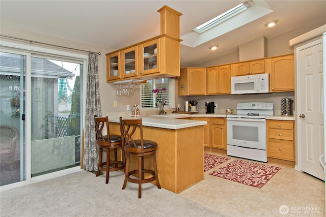 kitchen featuring a sink, white appliances, vaulted ceiling with skylight, a peninsula, and glass insert cabinets