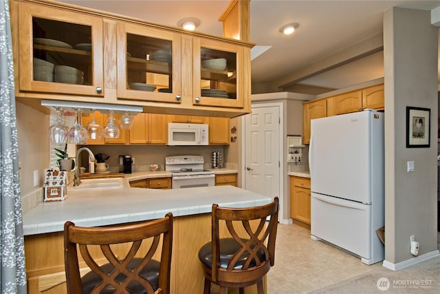 kitchen featuring glass insert cabinets, light countertops, a peninsula, white appliances, and a sink