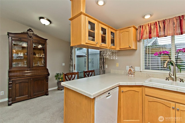 kitchen with white dishwasher, a sink, light countertops, glass insert cabinets, and light carpet