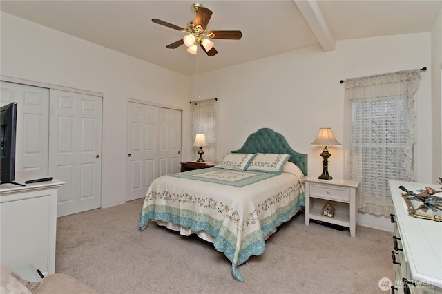 bedroom with beamed ceiling, a ceiling fan, multiple closets, and light carpet