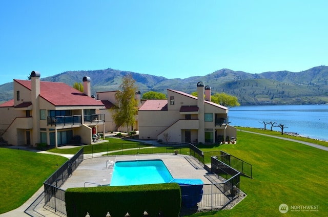 community pool featuring a water and mountain view, a lawn, and fence