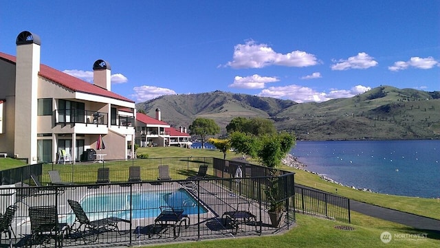 community pool with a patio area, a yard, fence, and a water and mountain view