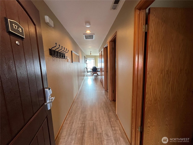 corridor with baseboards, visible vents, and light wood finished floors