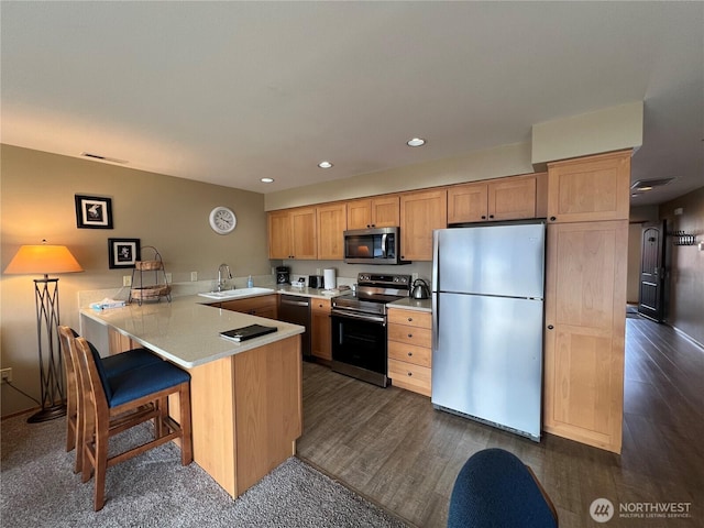 kitchen featuring a sink, light countertops, a peninsula, stainless steel appliances, and dark wood-style flooring