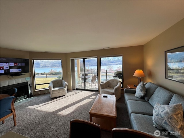 living area featuring visible vents, a fireplace with flush hearth, and carpet floors