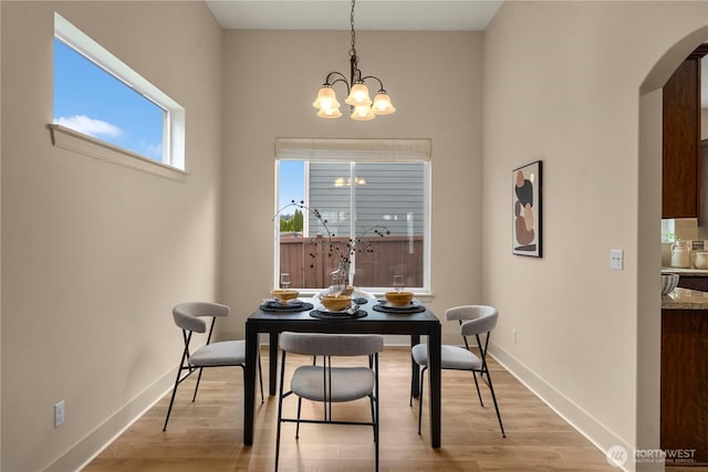 dining space with baseboards, arched walkways, light wood-style floors, and an inviting chandelier