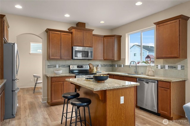 kitchen with a sink, light wood-type flooring, a kitchen bar, and appliances with stainless steel finishes