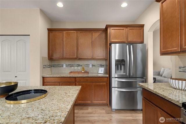 kitchen featuring light wood-style floors, tasteful backsplash, brown cabinetry, and stainless steel refrigerator with ice dispenser