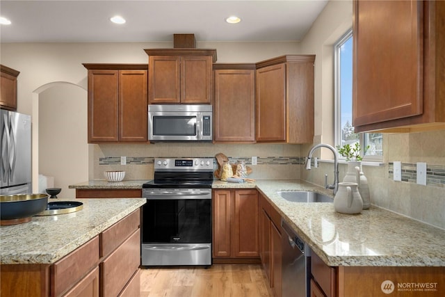 kitchen featuring light wood-style flooring, tasteful backsplash, appliances with stainless steel finishes, and a sink