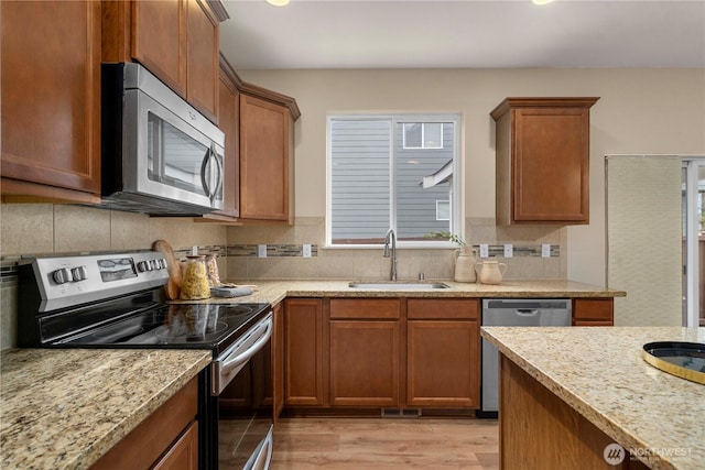 kitchen with brown cabinets, a sink, decorative backsplash, appliances with stainless steel finishes, and light wood-type flooring