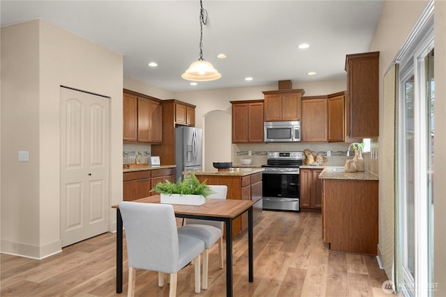 kitchen with light wood finished floors, a center island, recessed lighting, brown cabinets, and stainless steel appliances