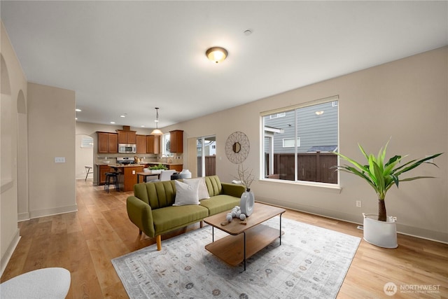 living room with recessed lighting, baseboards, arched walkways, and light wood finished floors