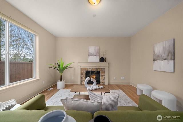 living room with a stone fireplace, visible vents, baseboards, and wood finished floors