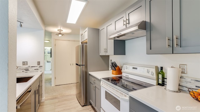 kitchen with under cabinet range hood, light countertops, decorative backsplash, gray cabinets, and appliances with stainless steel finishes