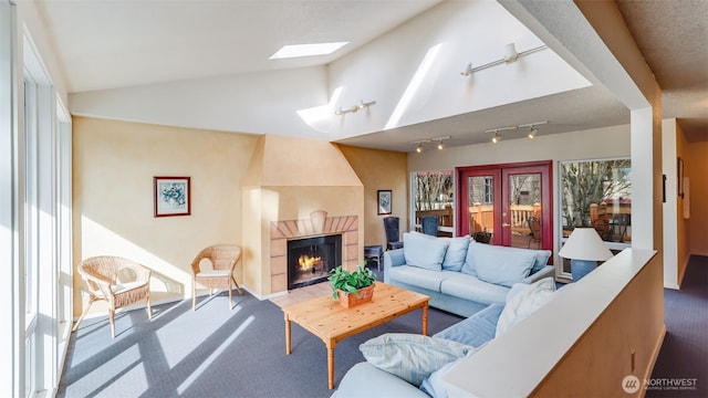 carpeted living area featuring rail lighting, vaulted ceiling with skylight, a healthy amount of sunlight, and a tiled fireplace