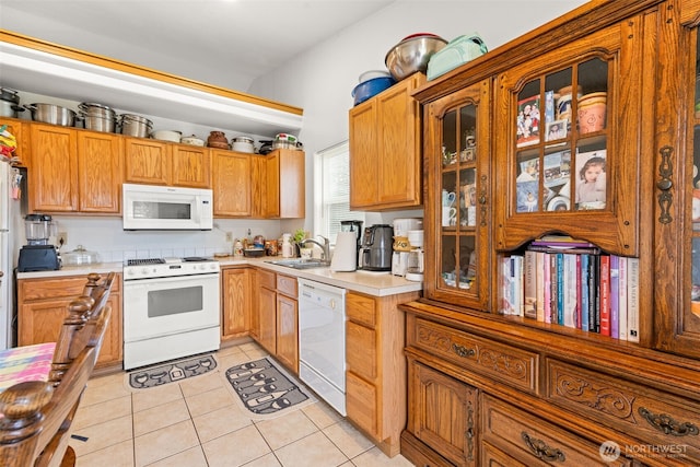 kitchen featuring light tile patterned flooring, white appliances, glass insert cabinets, light countertops, and a sink