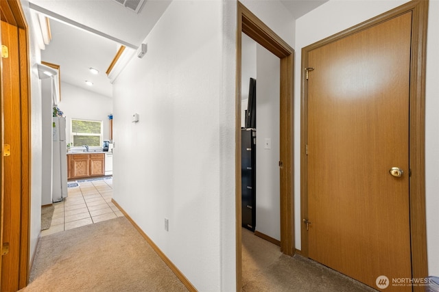 corridor featuring baseboards, light colored carpet, light tile patterned floors, and lofted ceiling