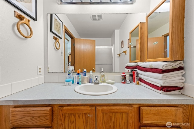 bathroom with a shower with door, visible vents, and vanity