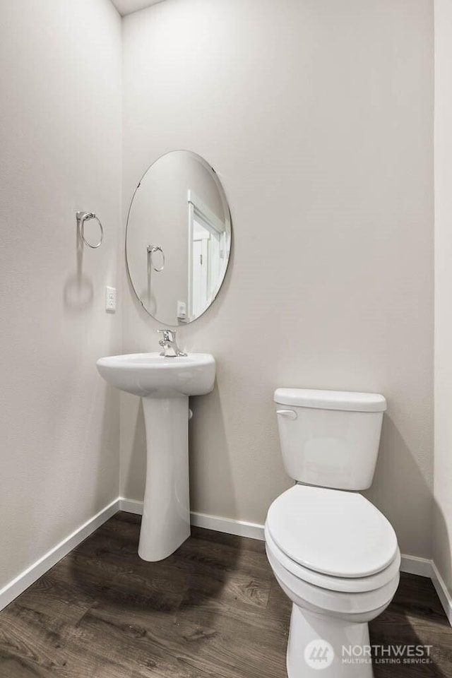 half bath with a sink, toilet, baseboards, and wood finished floors